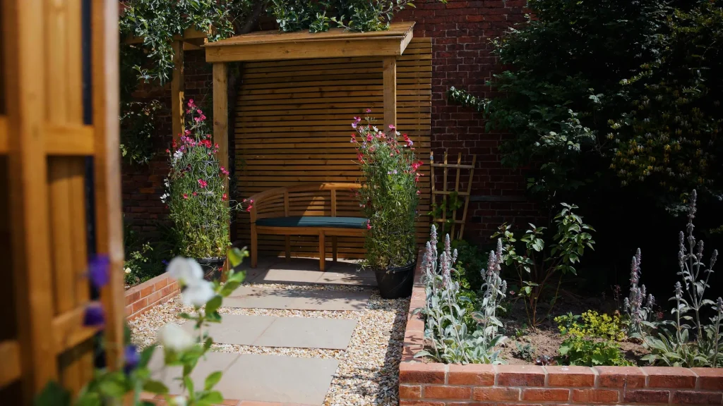 Timber arbour seating area set against a brick wall with raised brick planters in a traditional country garden in Retford.